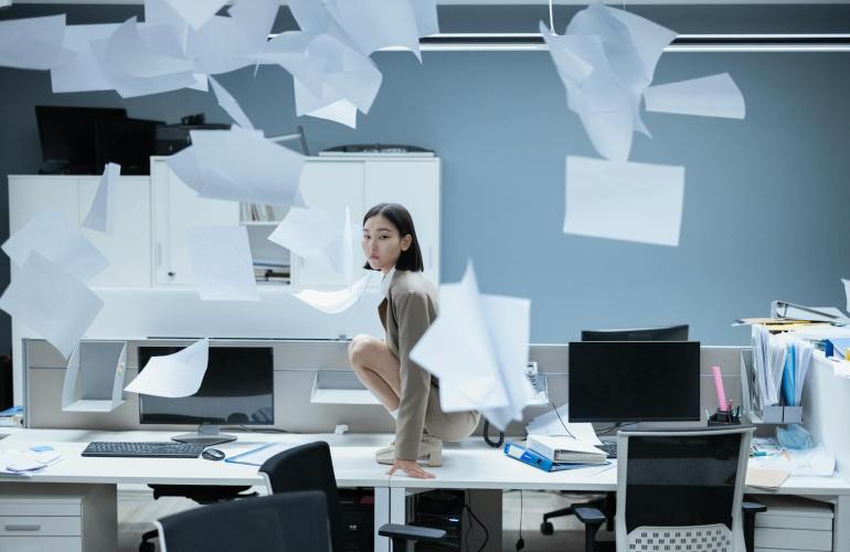 woman crouching on desk among flying papers in office